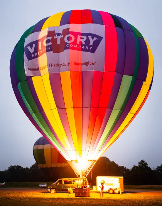 A hot air balloon is lit up by the light of a vehicle.