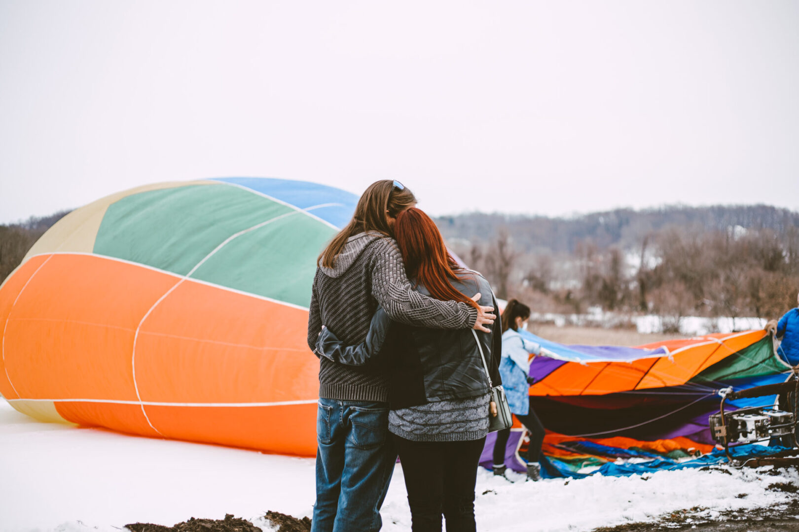 Two people hug in front of a hot air balloon.
