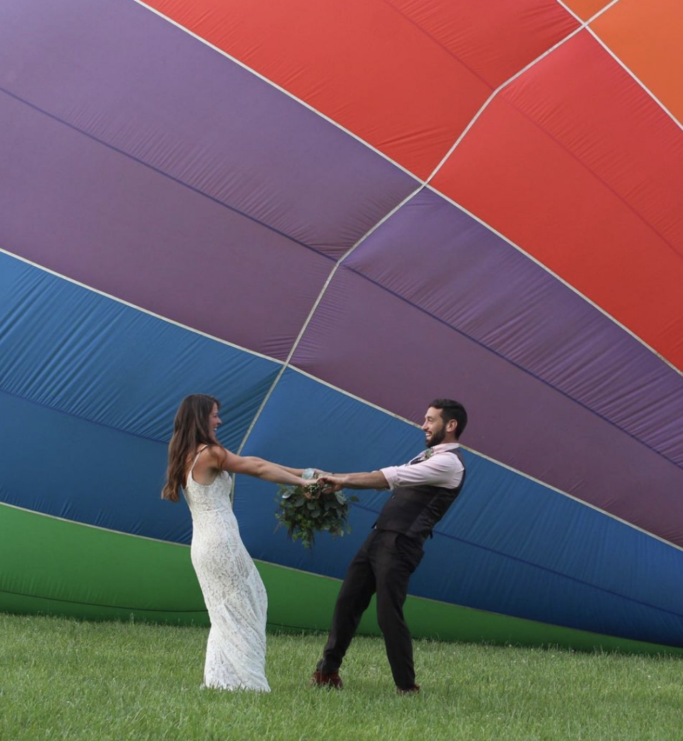 A man and woman holding hands in front of an air balloon.